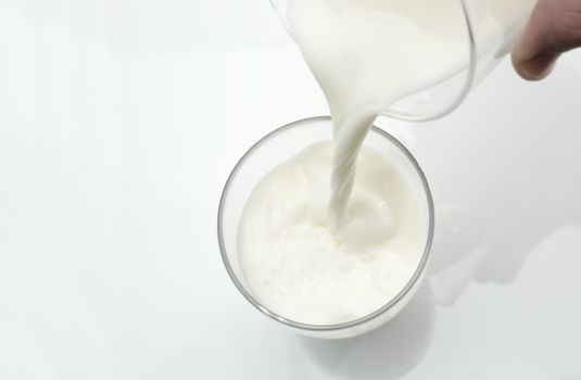 Person pours a glass of fresh milk against a white background.