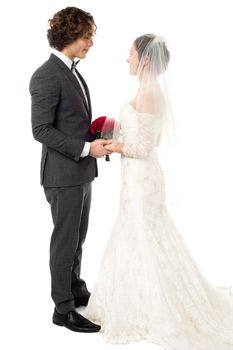 Studio shot of a couple in bridal attire facing each other and holding hands