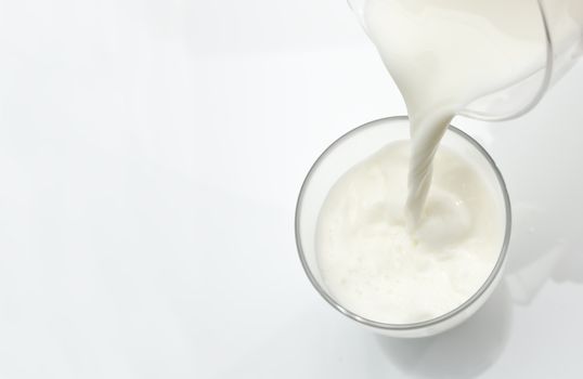 Pouring a glass of fresh milk against a white background.