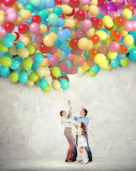 Image of happy family holding bunch of colorful balloons