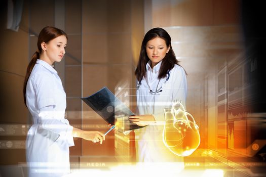 Image of two attractive women cardiologist examining virtual heart