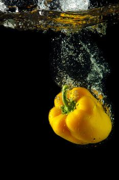 Colored yellow paprika in water splashes on black background