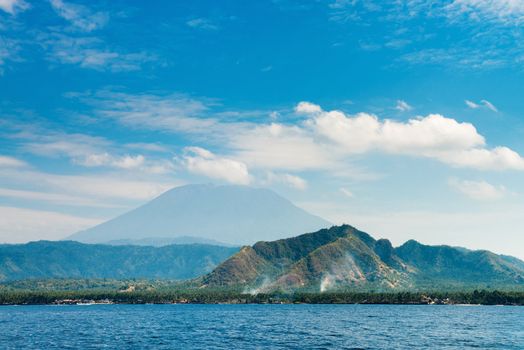 Gunung Agung the highest volcano on Bali island, Indonesia with blue cloudy sky and sea on front.