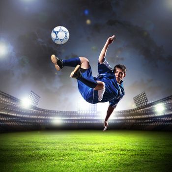 football player in blue shirt striking the ball aloft at the stadium
