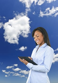 Smiling black woman with tablet computer over clouds and blue sky
