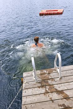 Teen girl splashing and swimming in lake near dock