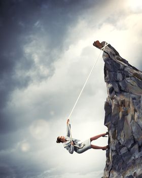 businesswoman climbing steep mountain hanging on rope