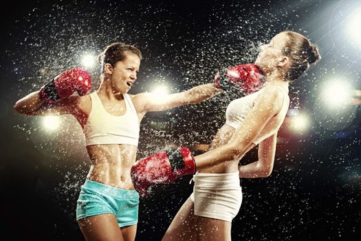 Two young pretty women boxing standing against flashes background