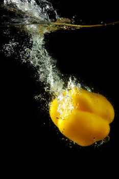 Colored yellow paprika in water splashes on black background