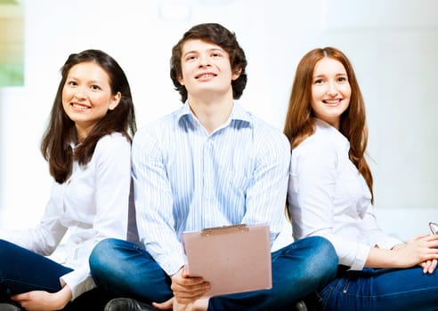 Image of three students in casual wear sitting on floor and smiling