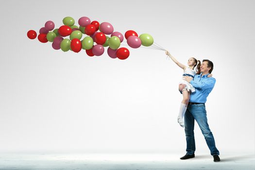 Image of happy father holding on hands daughter and balloons