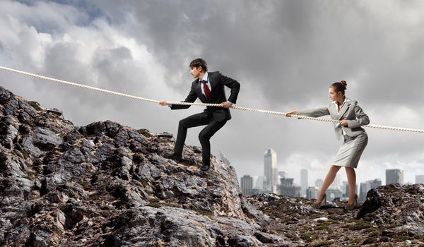 Image of busionessman and businesswoman pulling rope atop of mountain