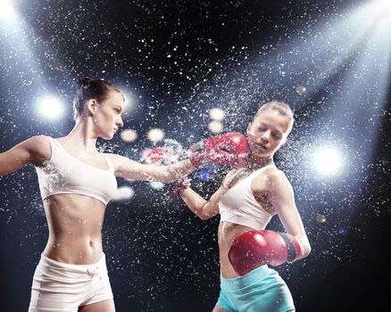 Two young pretty women boxing standing against flashes background