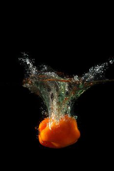 Colored orange paprika in water splashes on black background