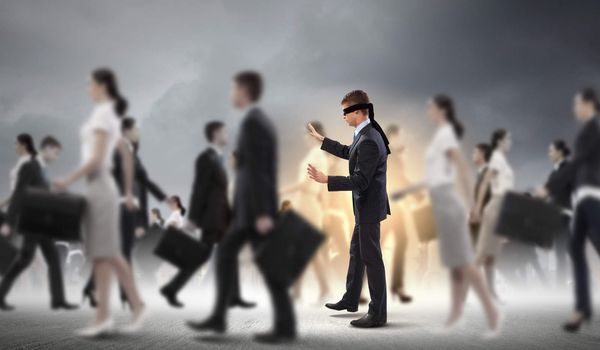 Image of businessman in blindfold walking among group of people