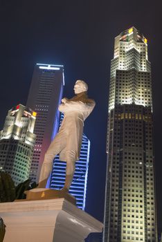 Tourism landmark symbol of Singapore, Sir Stamford Raffles statue with dramatic lighting at night with skyscrapers on background
