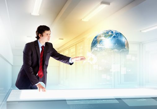 Image of young businessman clicking icon on high-tech picture of globe