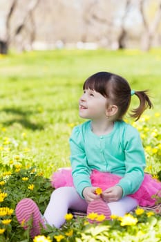 little girl sits on a glade among flowers and looks up