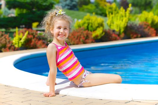 Pretty little girl sitting near swimming pool