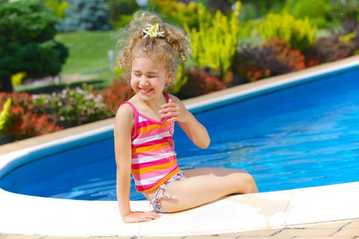 Pretty little girl sitting near swimming pool