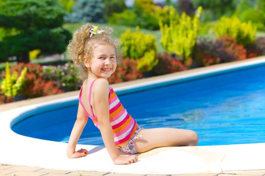 Pretty little girl sitting near swimming pool