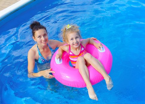 Pretty little girl in an pink life preserver with her mother in swimming pool outdoors