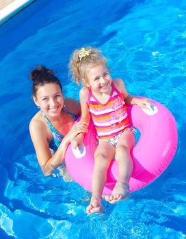 Pretty little girl in an pink life preserver with her mother in swimming pool outdoors. Vertical view.