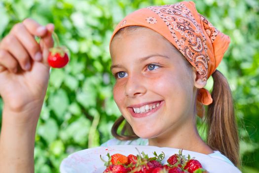 Beautiful little smiling girl eating strawberries in garden