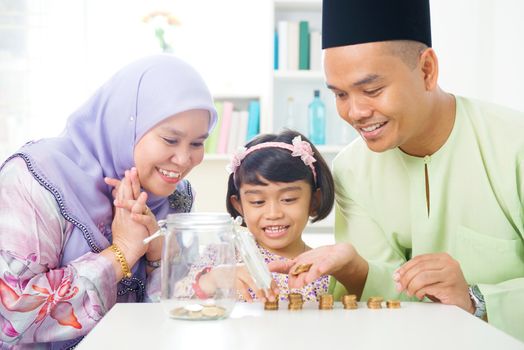 Islamic banking concept. Southeast Asian family counting money at home. Little Malay girl and parents saving money. Muslim father, mother and daughter living lifestyle.