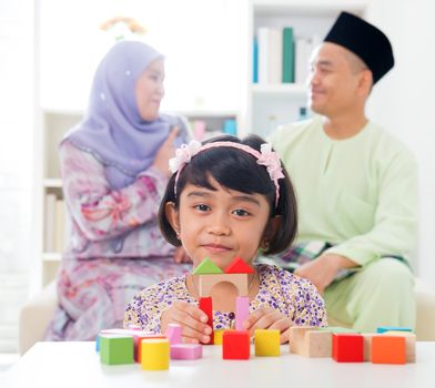 Malay girl building a wooden toy house. Southeast Asian family at home. Muslim parents and child living lifestyle.