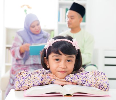 Muslim girl reading book. Malay family at home. Southeast Asian parents and child living lifestyle.