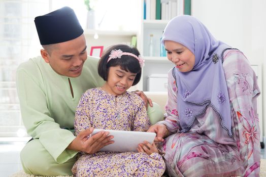 Southeast Asian family using tablet pc computer at home. Muslim family living lifestyle. Happy smiling Malay parents and child.