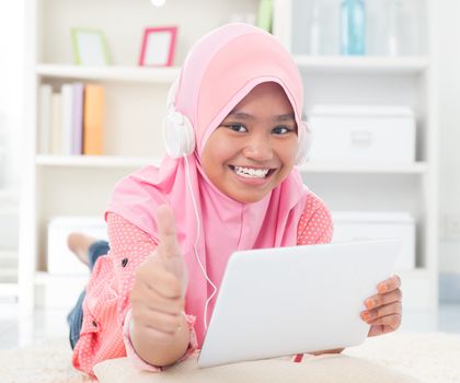 Asian teen listening to music with headphone and thumb up. Southeast Asian teenager at home. Muslim teenage girl living lifestyle.