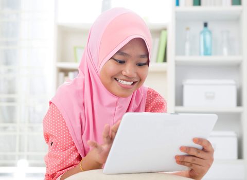 Asian teen using tablet pc computer. Southeast Asian teenager at home. Muslim teenage girl living lifestyle.