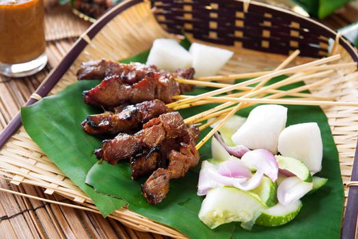 Satay or sate, skewered and grilled meat, served with peanut sauce, cucumber and ketupat, Malaysia or Indonesia food. Traditional Malay food. Hot and spicy Malaysian dish, Asian cuisine.