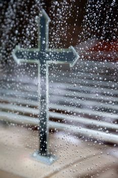 cross seen through hearse window full of raindrops