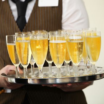 Closeup view of the hands of a waiter carrying a tray of champagne in tall elegant flutes at a wedding reception or catered event