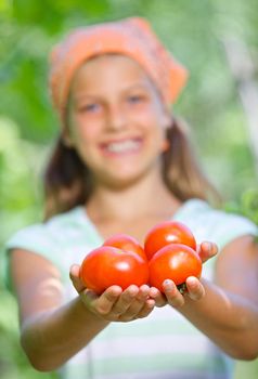 Portrait of beautiful girl holding tomatoes in green garden. Focus on the tomatoes.