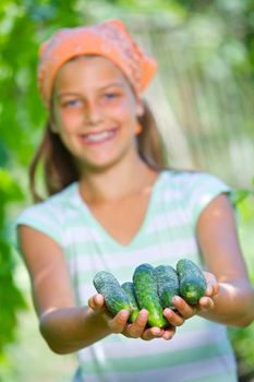 Portrait of beautiful girl holding cucumbers in green garden. Focus on the cucumbers.