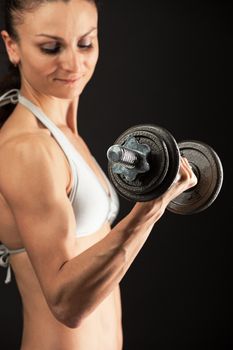 Muscular young woman lifting a dumbbell over black