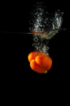 Colored orange paprika in water splashes on black background