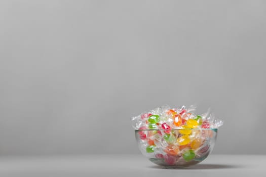 Colour fruit candy in a crystal vase on a gray background