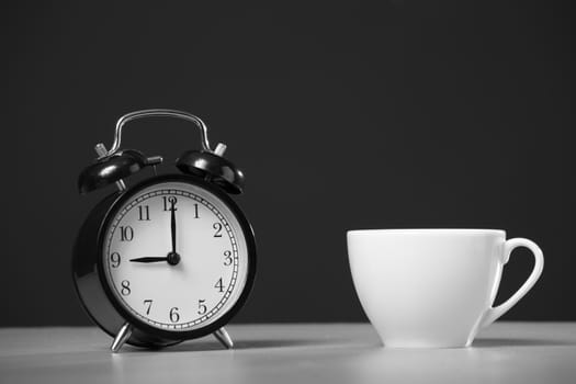 Cup of coffee and alarm clock on a black background.