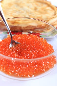 red caviar in a plate with the spoon and pancakes on a background