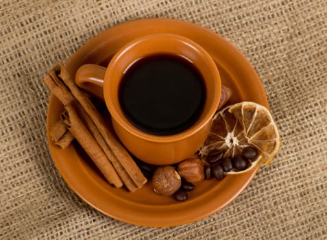 Closeup shot of freshly prepared cup of italian espresso with cinnamon, coffe beans, nuts and lemon over sacking