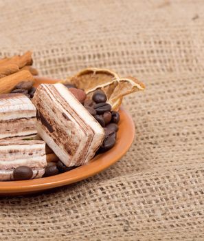 Sweets, cinnamon, nuts and coffee beans on a saucer, on burlap background.