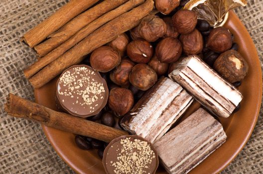 Sweets, cinnamon, nuts and coffee beans on a saucer, on burlap background.