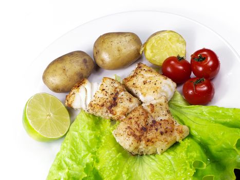 Fried white fish on a plate, with potatoes, lettuce, lime and tomatoes