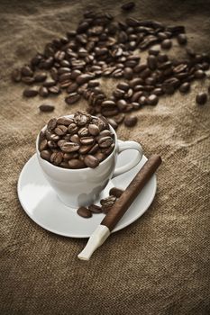 cup with coffee beans and cigar on burlap