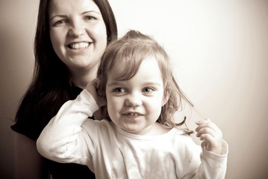 Toddler age girl sitting with her smiling mother. Sepia tone.